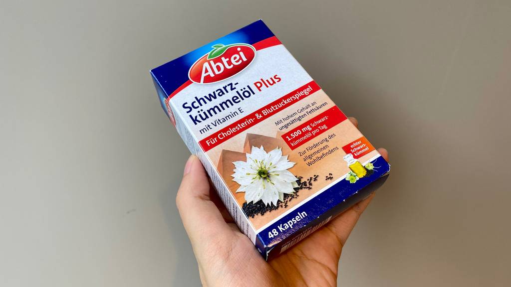 Schwarzkümmelöl-Kapseln getestet: Eine Hand hält eine Packung Kapseln vor einen grauen Hintergrund