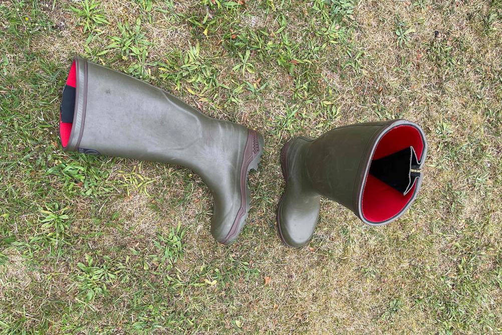 Neopren-Gummistiefel im Test, einer liegend und einer stehend in einer Wiese.