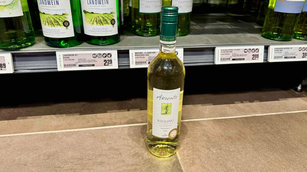 Eine Flasche getesteter Riesling steht vor einem Regal, bei welchem man die Preisschilder sieht.