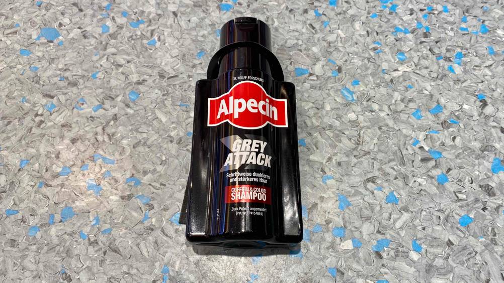 Eine Flasche des getesteten Shampoos gegen graue Haare auf einer grauen Fläche.