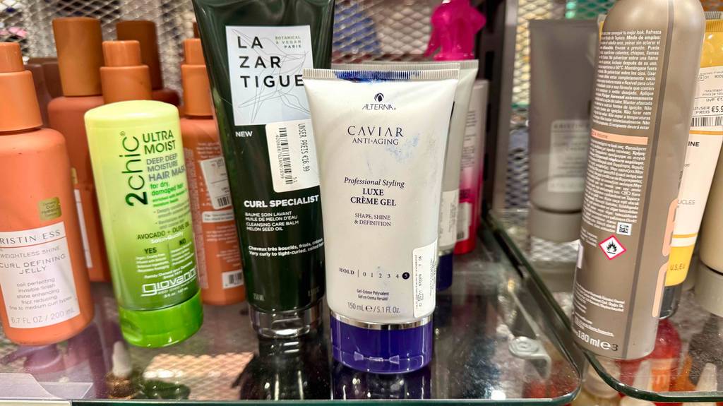 Eine getestete Styling-Creme steht auf einer Glasoberfläche neben anderen Produkten.