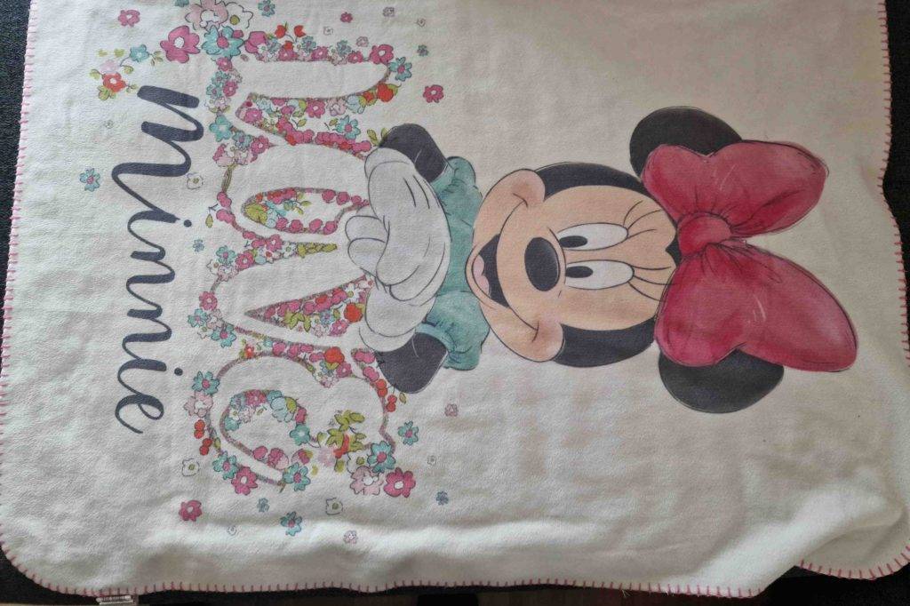 Auf einem Boden liegt eine getestete Babydecke mit Minnie Maus als Motiv.