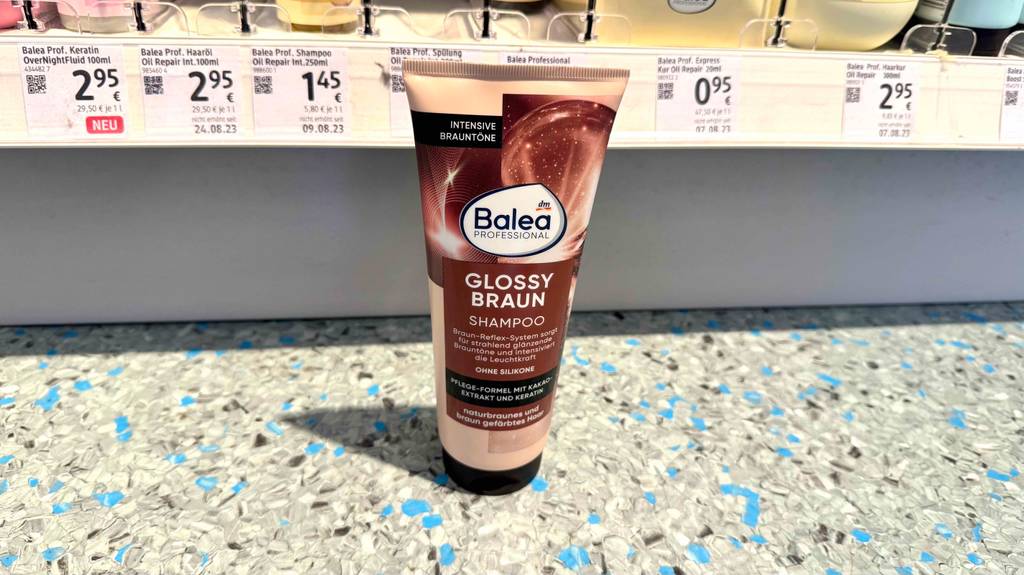 Eine getestete Flasche Color-Shampoo-Braun steht vor einem Regal.