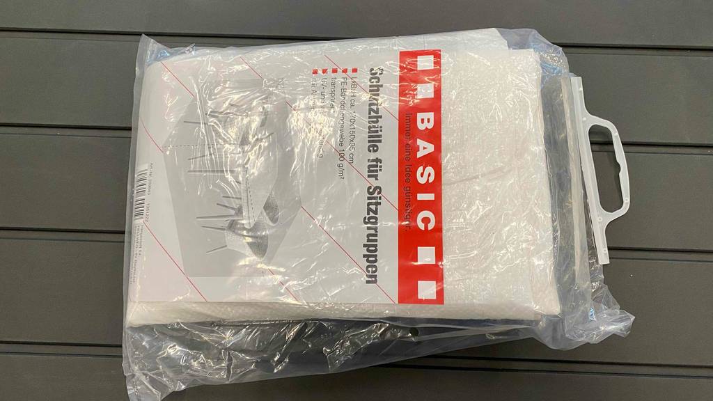 Gartenmöbel-Abdeckung im Test: eine Schutzhülle für Sitzgruppen, liegt in der Verpackung auf einem grauen Untergrund.