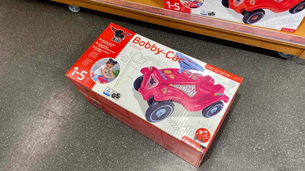 Bobby-Car-Test: Die Verpackung eines Bobby-Cars liegt auf einem Boden vor einem Regal.