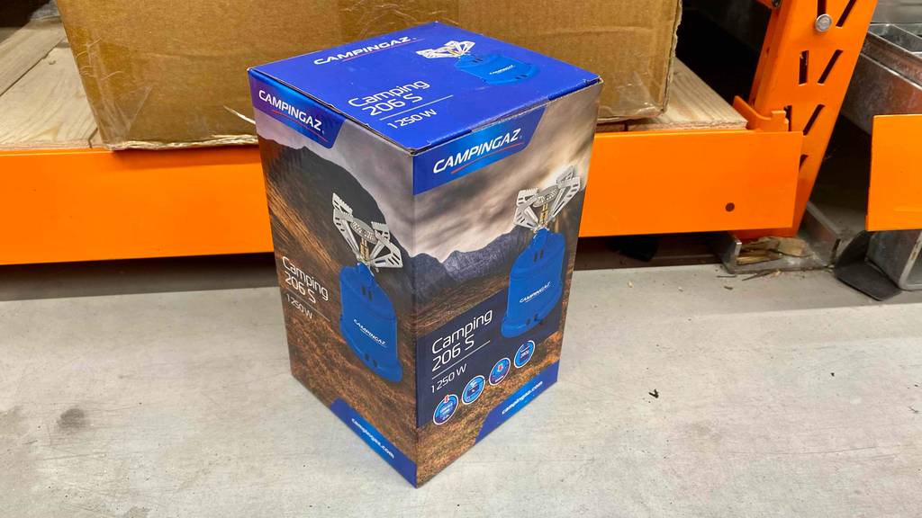 Ein getesteter Campingaz-Gaskocher in Verpackung steht vor einem Regal.