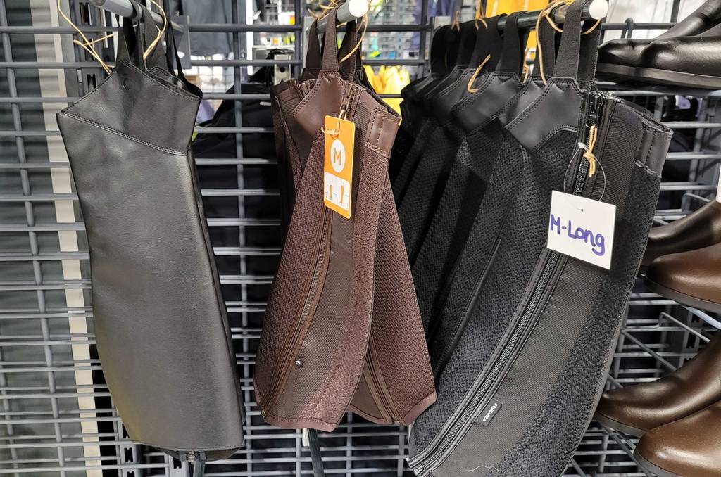 Getestete Reitchaps hängen in verschiedenen Farben in einem Regal, neben Schuhen.