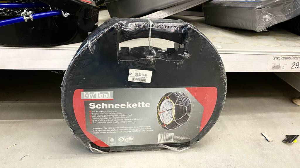 Eine getestete Schneekette in der Originalverpackung im stehenden Zustand vor einem Regal.