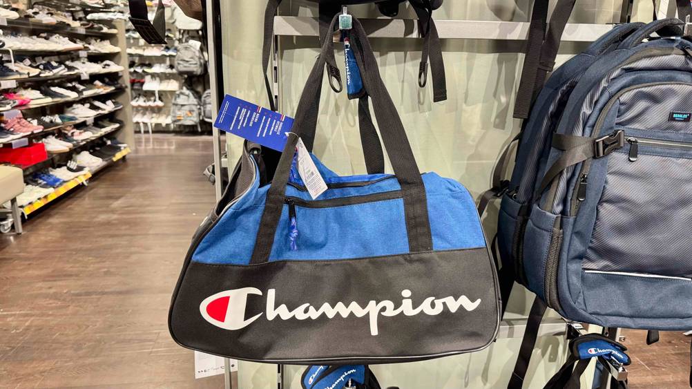 Die getestete Sporttasche von Champion hängt auf einem Haken neben einem Rucksack in einem Geschäft.