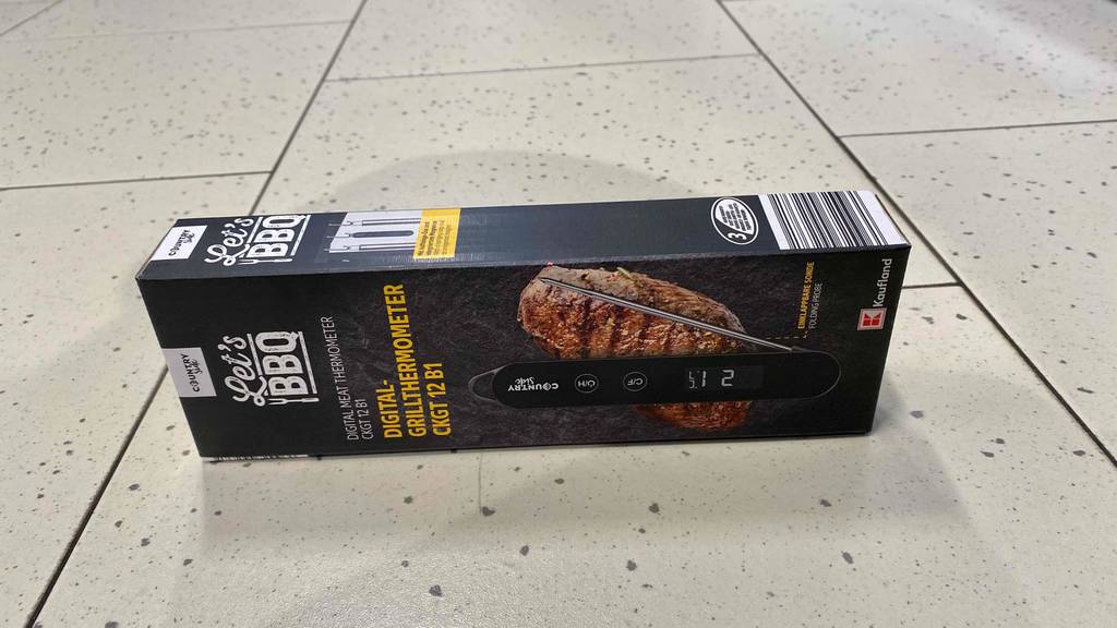 Auf einem Fließenboden liegt horizontal eine Packung des getesteten Grillthermometers auf der Seite.