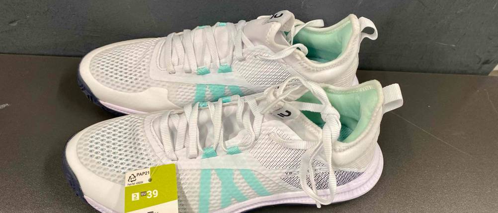 Volleyballschuhe für Damen getestet: Ein Paar weiße Schuhe mit türkisfarbenen Streifen, von der Seite auf einer grauen Fläche aufgenommen.