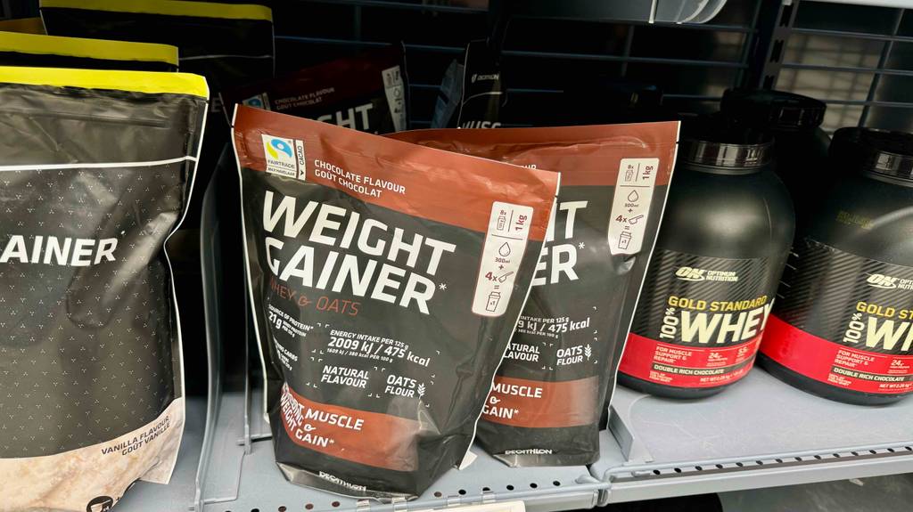 Getestet: mehrere Packungen Weight Gainer stehen in einem Regal neben andere Produkte.