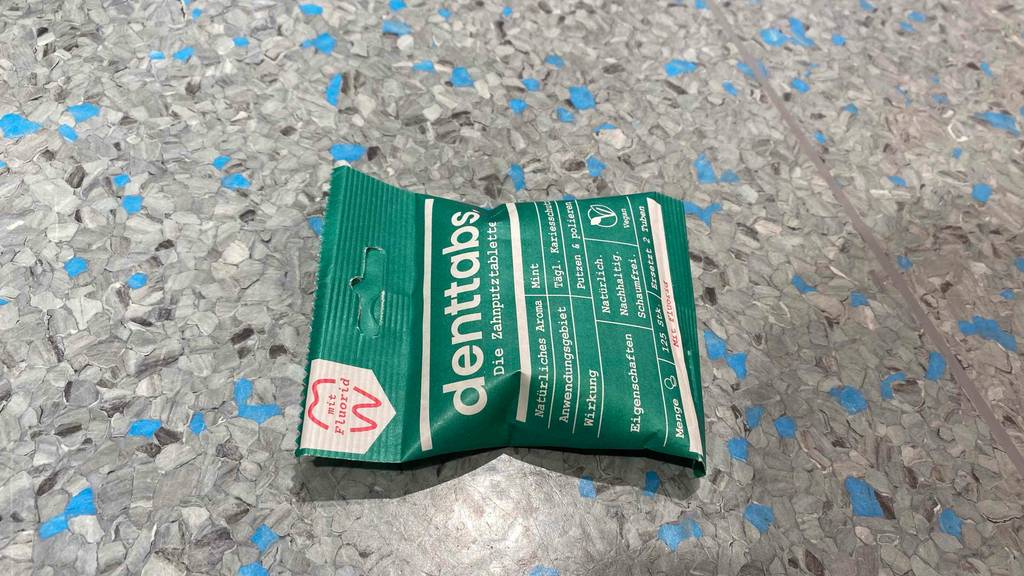 Eine Packung der getesteten Zahnputztabletten horizontal auf einer grauen Fläche.