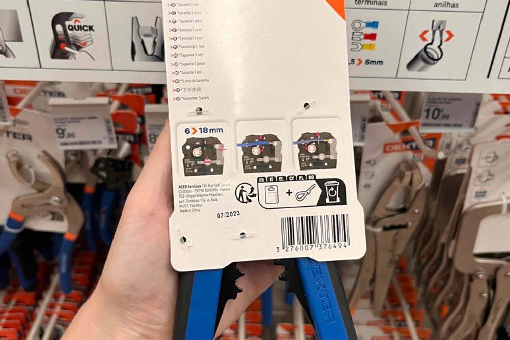 Automatische-Abisolierzange im Test: Abisolierzange wird eingepackt mit der Rückseite ersichtlich vor einem Regal gehalten.