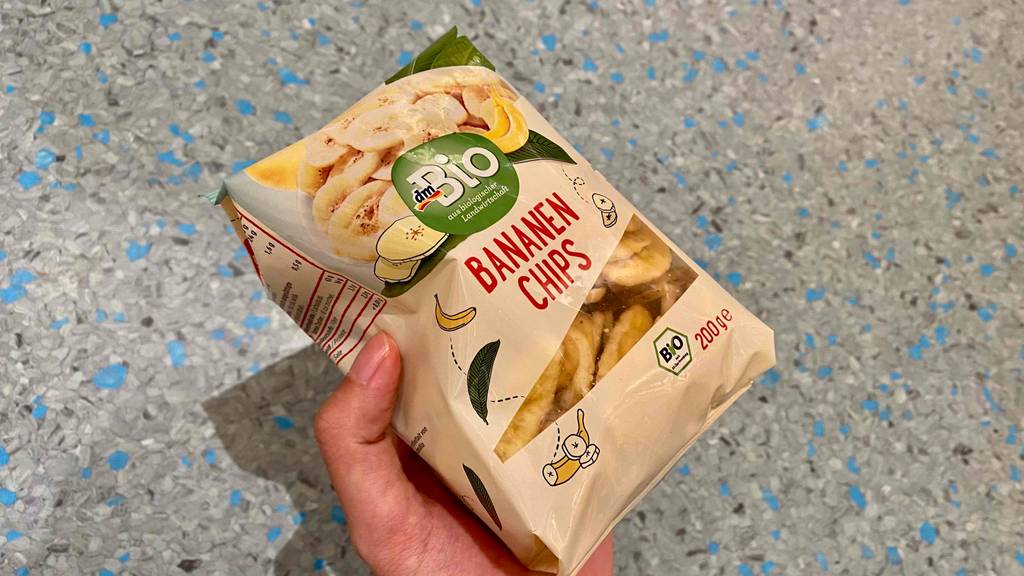 Bananenchips im Test: Eine Hand hält eine Packung Chips vor hellen Hintergrund