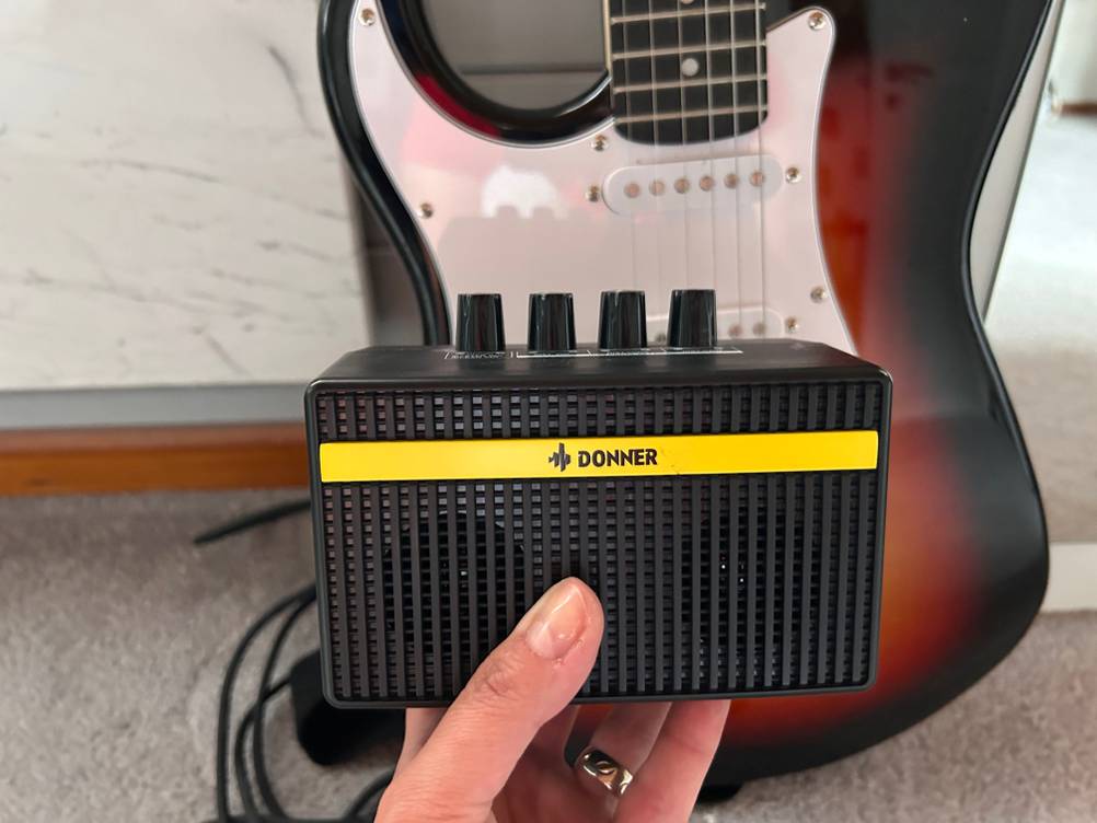 Miniverstärker im Test: Ein schwarzer Miniverstärker wird vor einer E-Gitarre gehalten.