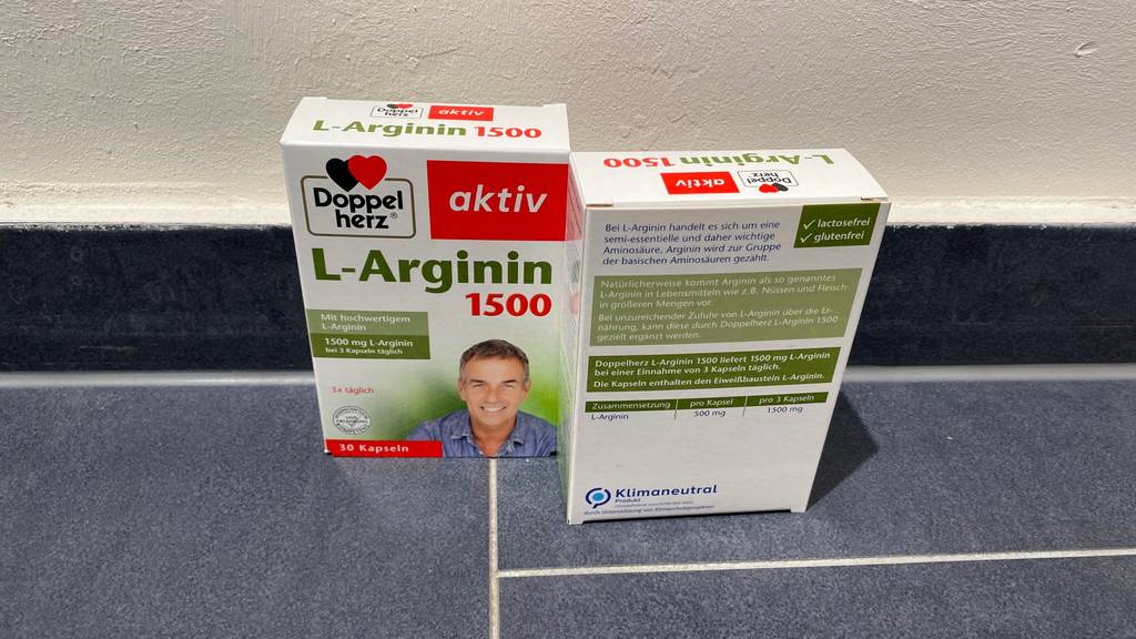 L-Arginin im Test: Zwei Packungen vor einer hellen Wand, eine Vorderseite, eine Rückseite