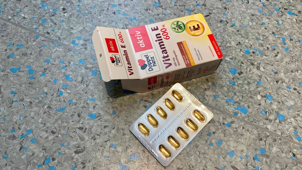 Vitamin E getestet: Eine Packung und eine einzelne Tablettenreihe nebeneinander auf Fließenboden