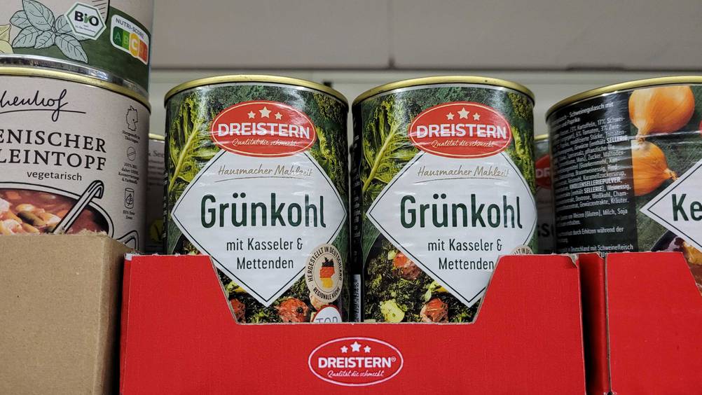 Mehrere Dosen des getesteten Gruenkohls nebeneinander in einem Karton im Regal