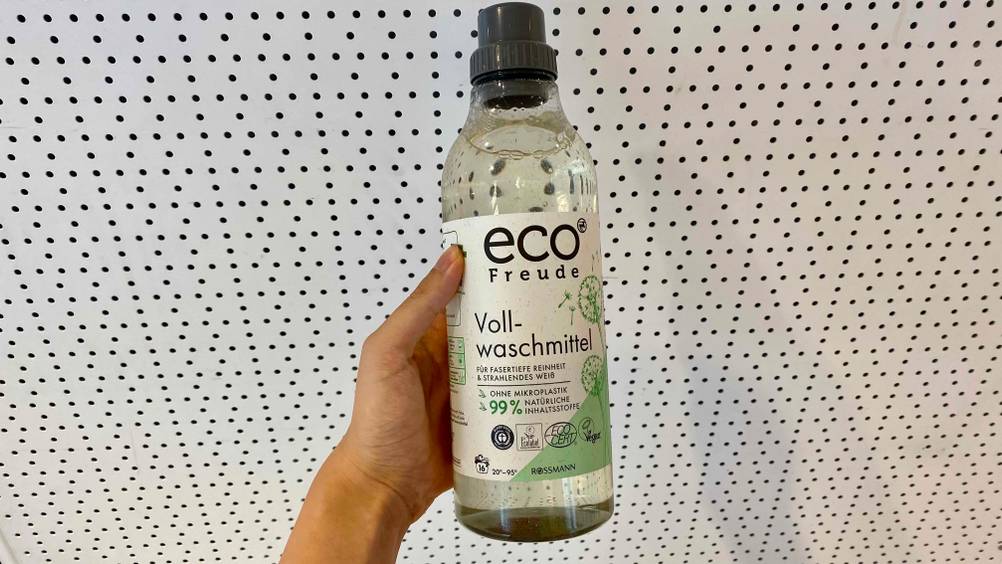 Vollwaschmittel im Test: Eine Hand hält eine Flasche vor eine helle Wand