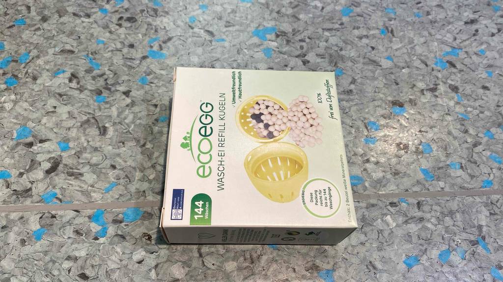 Eine getestete Waschkugel in ihrer Originalverpackung auf einem grauen Boden.