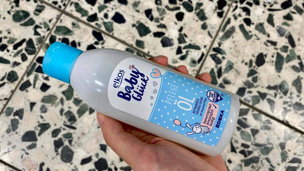 Babyöl getestet: Eine Hand hält eine Flasche Öl im Hintergrund ein Fließenboden