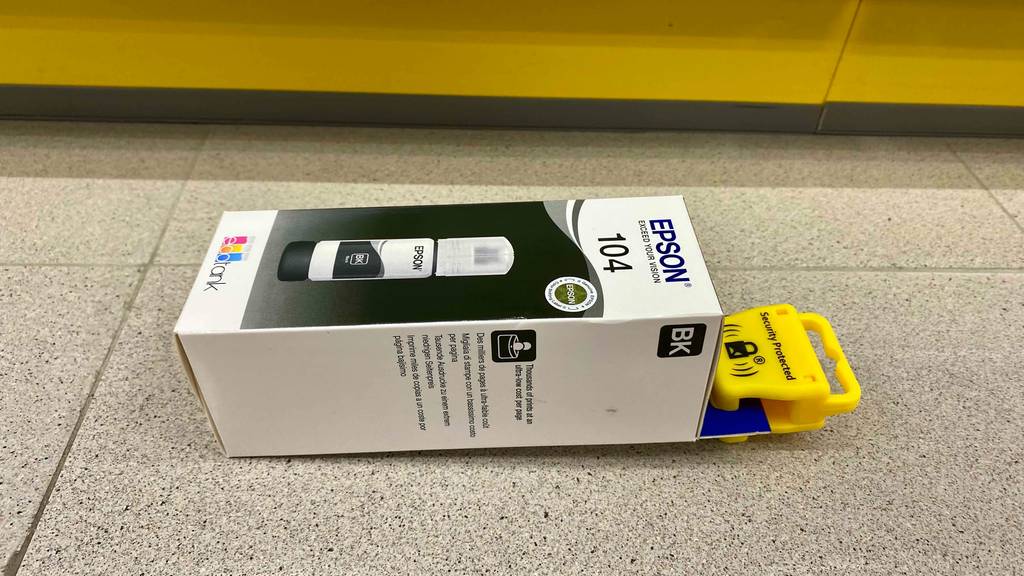 Ein getesteter Epson-EcoTank von der Seite auf einer grauen Fläche liegend.