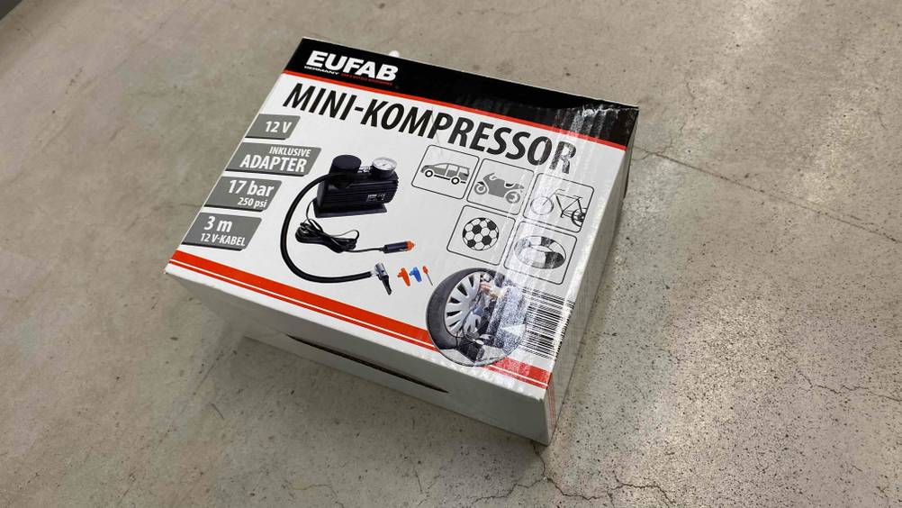 Eine Packung mit dem getesteten 12V-Kompressor liegt auf einem Betonboden.