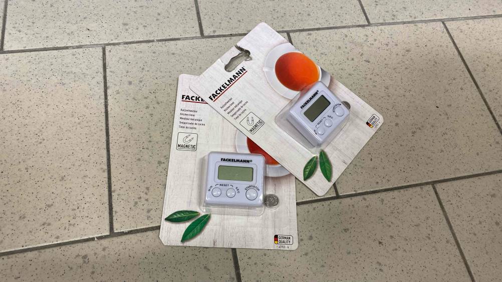 Auf einem hellen Boden liegen zwei getestete Kurzzeitwecker in Originalverpackung.