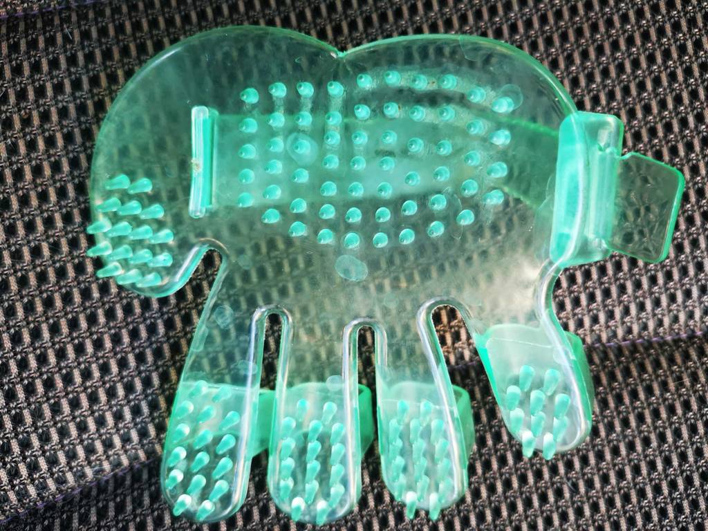 Im Test: Der Fellpflege-Handschuh mit Noppen liegt auf einem grauen Stoff.