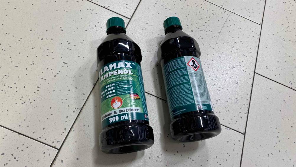 Lampenöl im Test: ein Lampenöl von der Rückseite ersichtlich am Boden liegend und daneben eine Flasche von der Vorderseite ersichtlich.