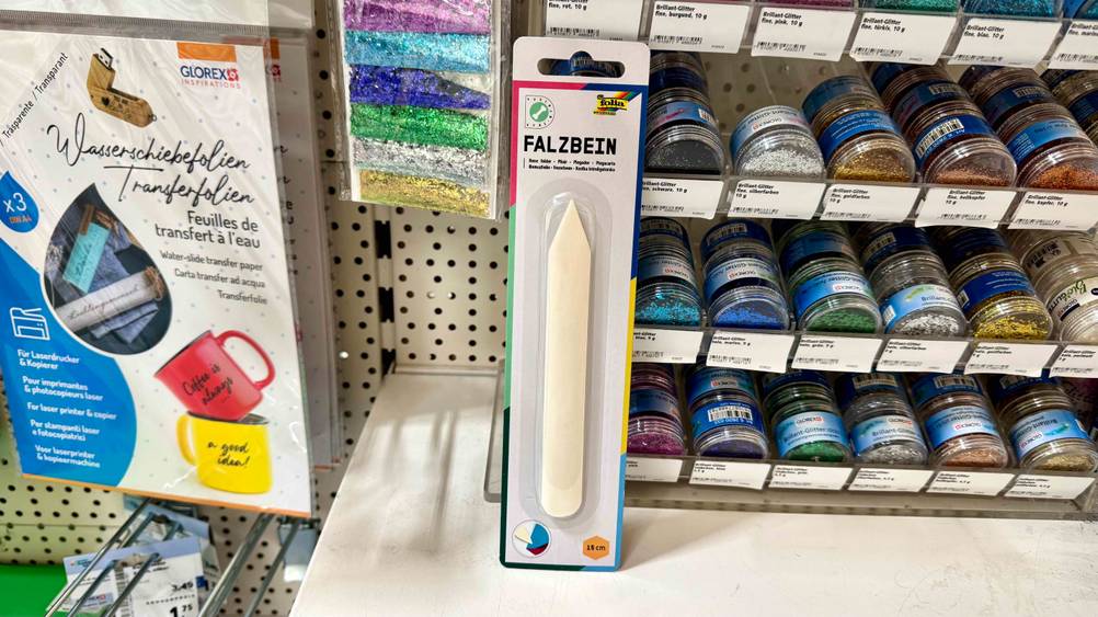 Ein getestetes Falzbein befindet sich in einem Regal neben Bastelzubehör.