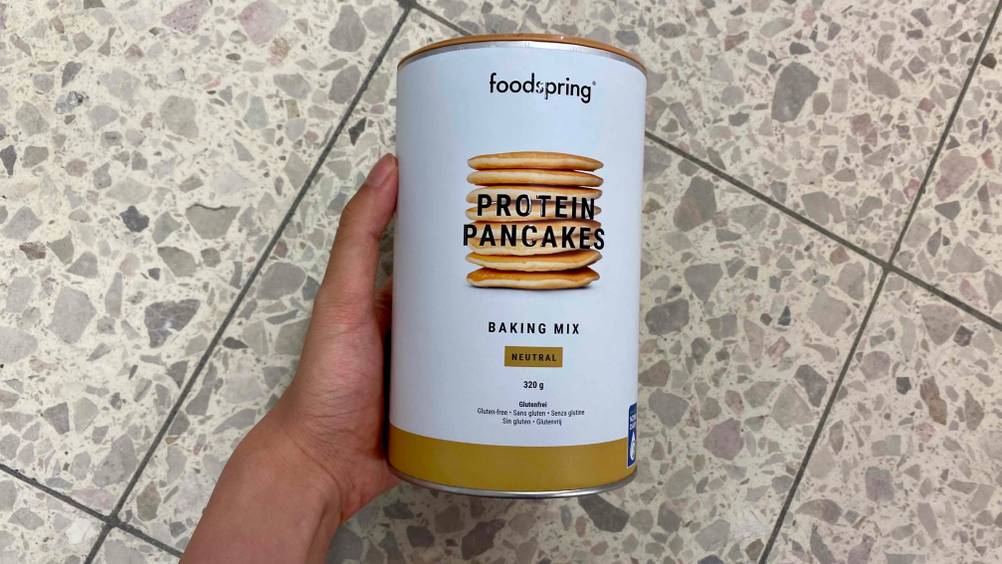 Protein Pancake im Test: Eine Hand hält eine Packung Pancake vor eine Fließenoberfläche