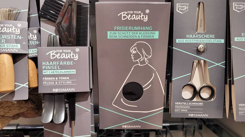 Ein getesteter Friseurumhang hängt in einem Regal neben anderen Utensilien.