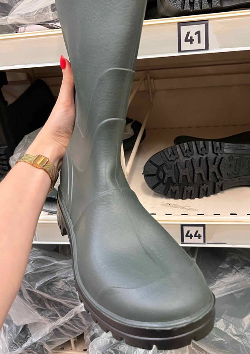 Gummistiefel-Herren getestet: grauer Gummistiefel von vorn wird vor einem Regal mit anderen Schuhen gehalten.