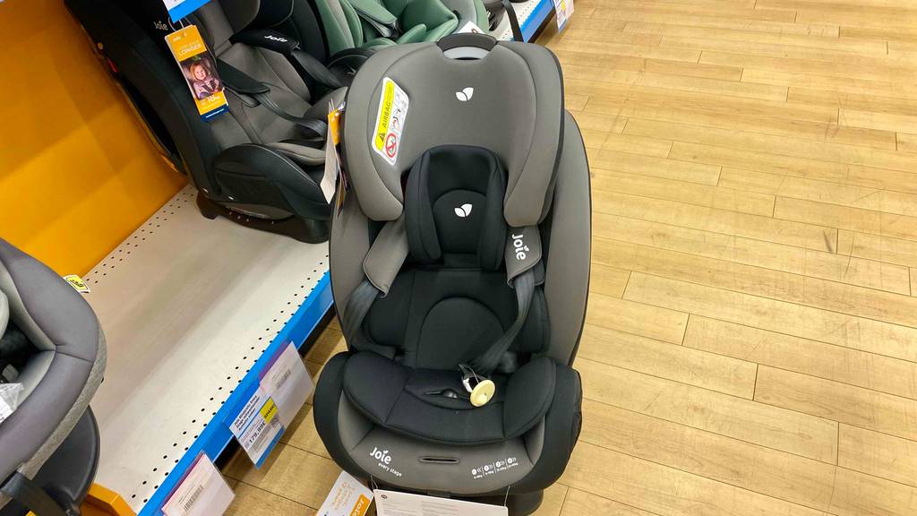 Ein getesteter Kindersitz 0–36 kg steht neben einem Regal mit anderen Sitzen auf einem Holzboden.