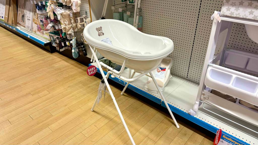 eine weiße getestete Babybadewanne mit Gestell, mit Motiv im Innenraum steht vor einem Regal.