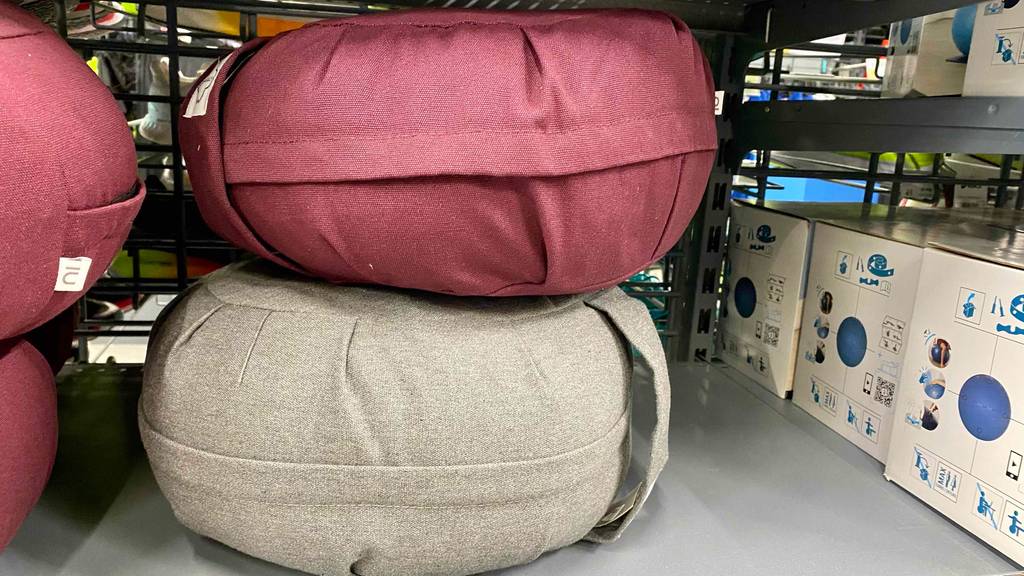 Meditationskissen im Test: ein rotes Meditationskissen ist auf einem beigen platziert, welche sich in einem Regal befinden.