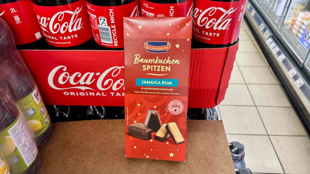 Baumkuchen-Test: Die Verpackung der Baumkuchen-Spitzen lehnen an einem Karton, worin sich Cola-Flaschen befinden.