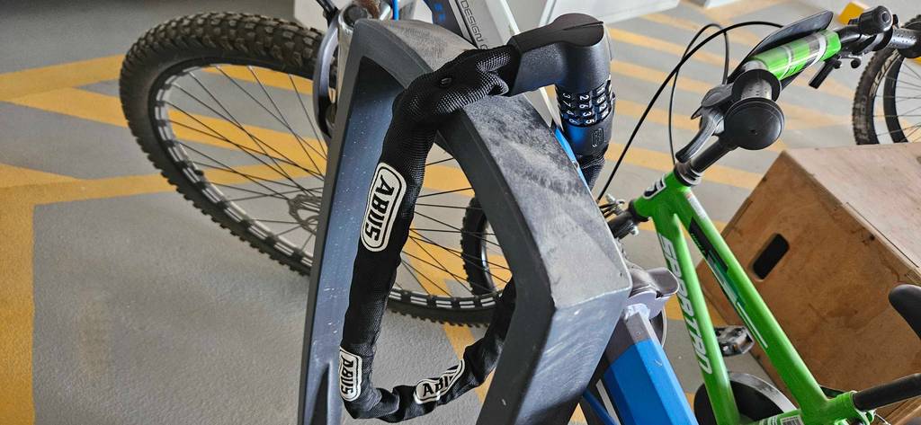 Fahrradschloss-lang-Test: Nahaufnahme eines getesteten langen Fahrradschlosses das ein Fahrrad an ein Gestänge festmacht.