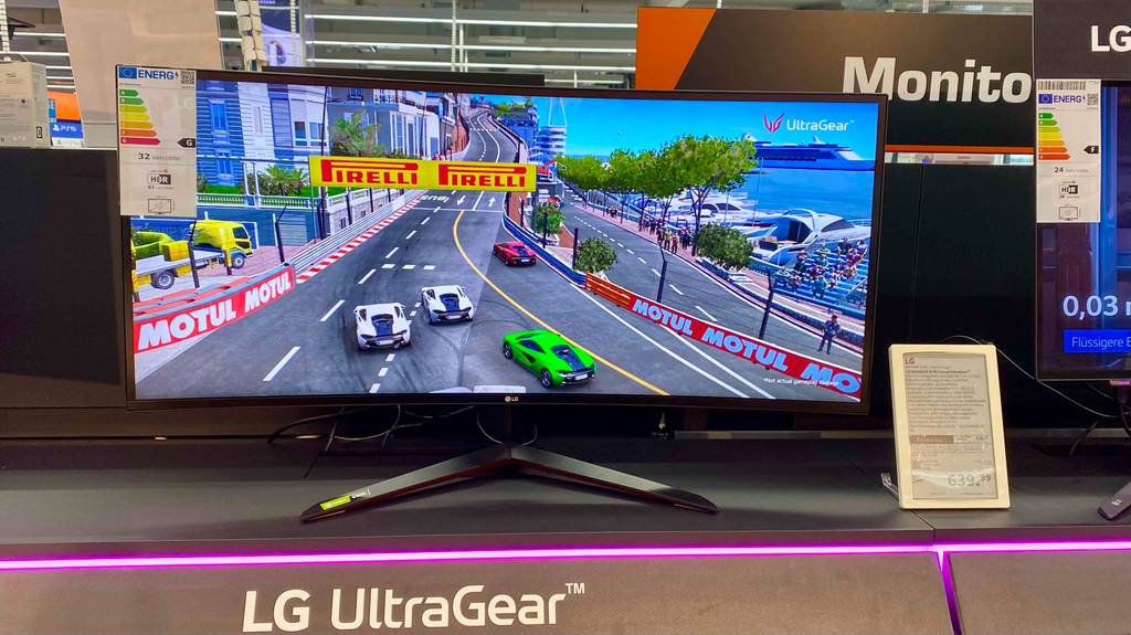 Ein eingeschalteter, getesteter Curved-Monitor mit 144 Hz steht in einemm Regal neben Informationsschild.