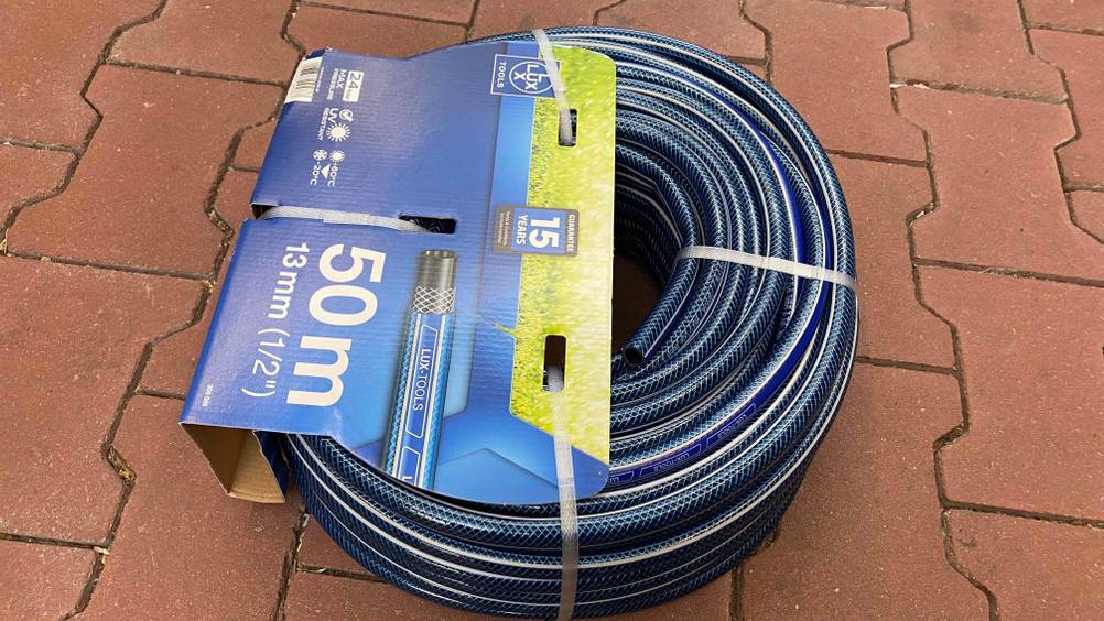 Gartenschlauch-50m getestet: Blauer Gartenschlauch noch verpackt auf einem roten Steinboden liegend, mit Informationen zu Produkt.