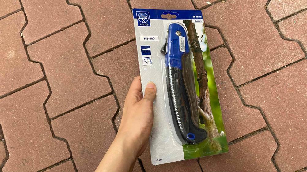 Klappsäge getestet: Klappsäge in Verpackung wird vor einem roten Steinboden gehalten.