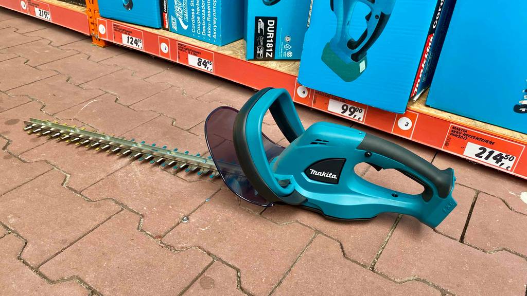 Makita-Akku-Heckenschere getestet: eine Makita-Akku-Heckenschere steht auf einem Boden vor einem Regal.