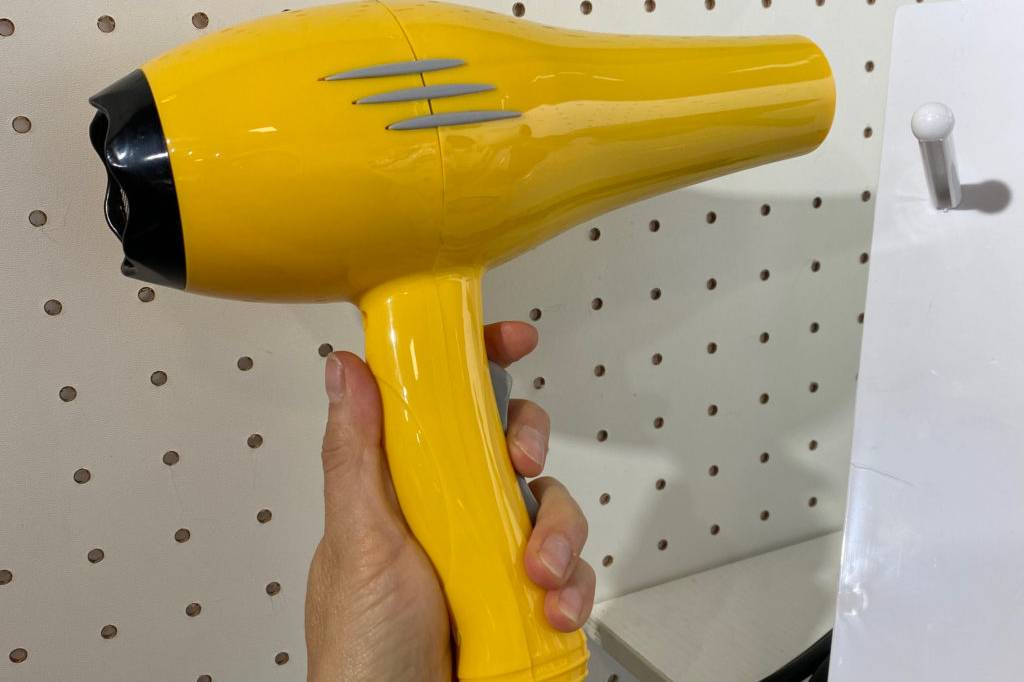 Profi Haartrockner im Test: Eine Hand hält einen gelben Haartrockner vor eine Lochplatte