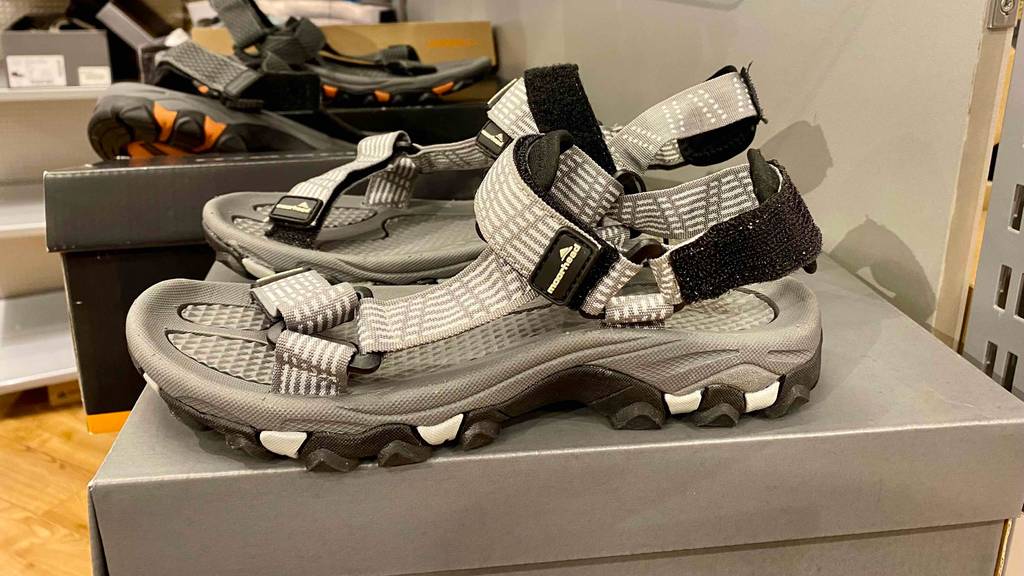 Auf einem Karton neben anderen Produkten steht ein Paar getestete Unisex-Trekkingsandalen.