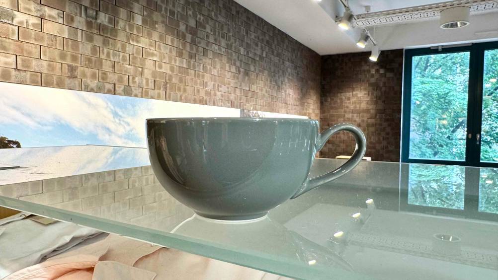 Eine graue getestete Teetasse steht auf einer Glasfläche.