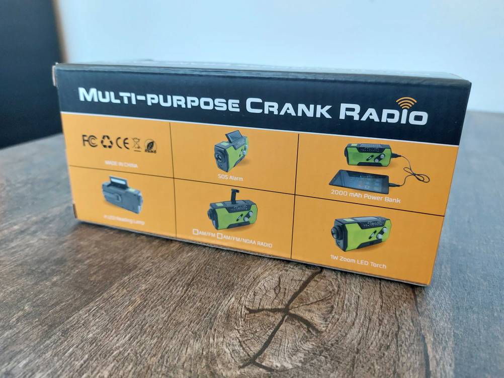 Ein getestetes Kurbelradio in Originalverpackung auf einem Holzfisch.