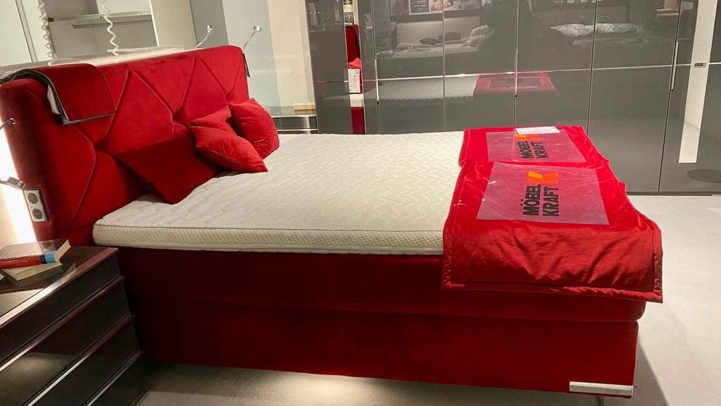 Boxspringbett-160x200 im Test: ein rotes Boxspringbett mit Kissen darauf von der Seite ersichtlich.