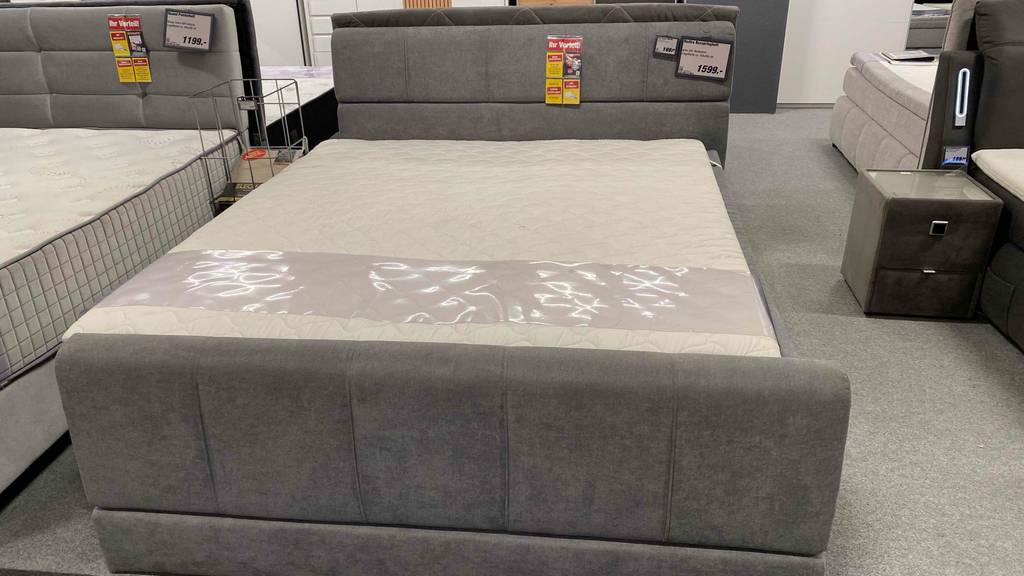 Boxspringbett-180x200 im Test: ein graues Boxspringbett, bei welchem man den Fußteil und den Kopfteil sehen kann.